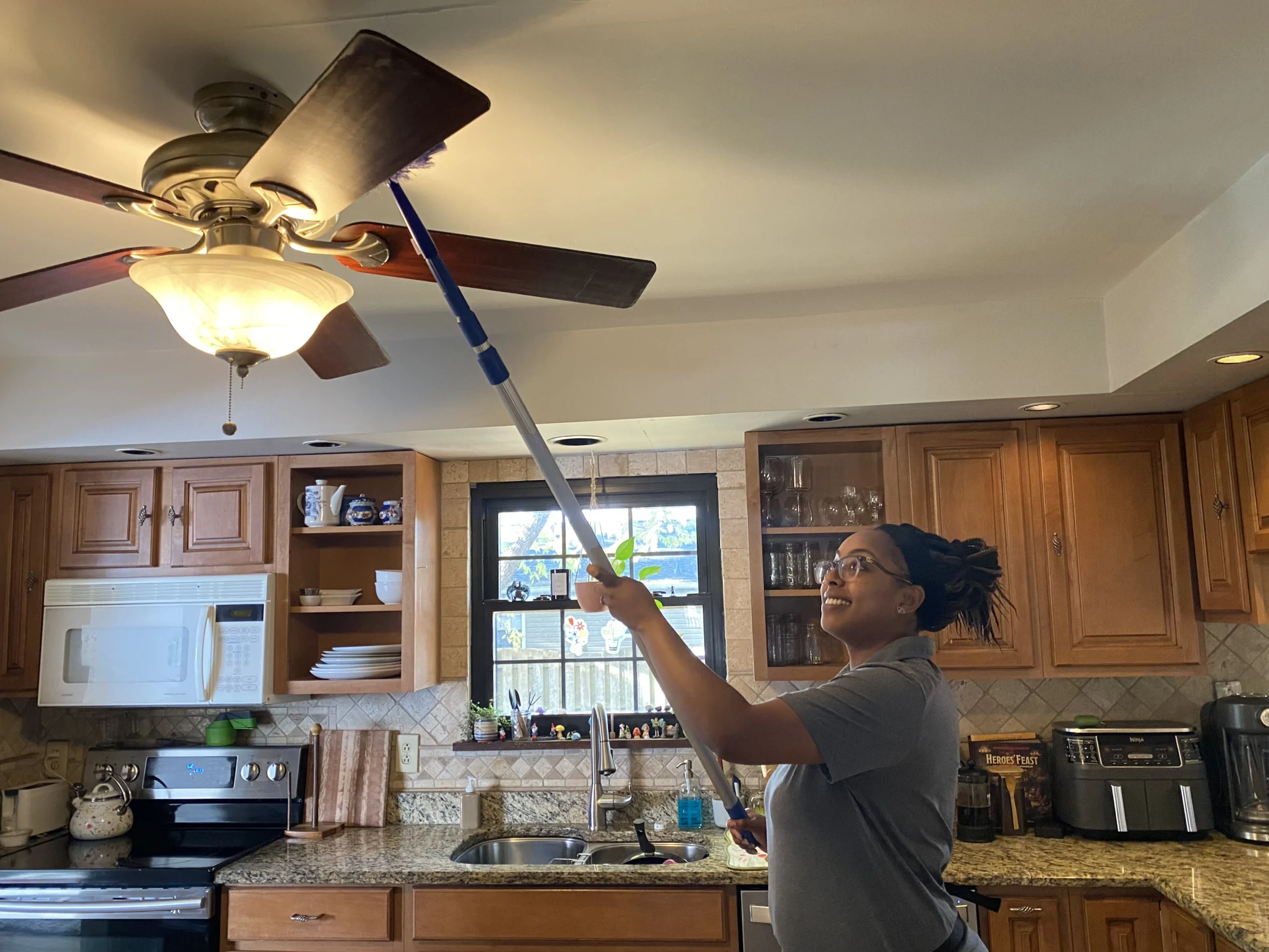 Cleaning specialist dusting ceiling fan in kitchen as part of thorough move-out cleaning service.